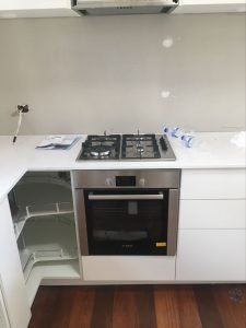 kitchen install in progress with stainless steel cook top and oven awaiting doors to be attached on cabinetry