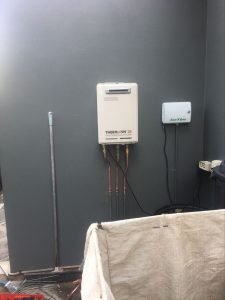 Thermann hot water system attached to a grey wall beside small rectangular white irrigation system