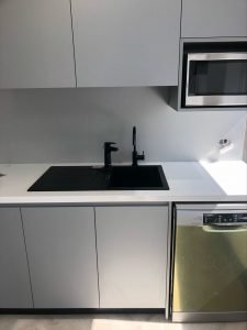 newly installed commercial kitchen with black tapwear, a microwave and dishwasher in white and grey cabinetry