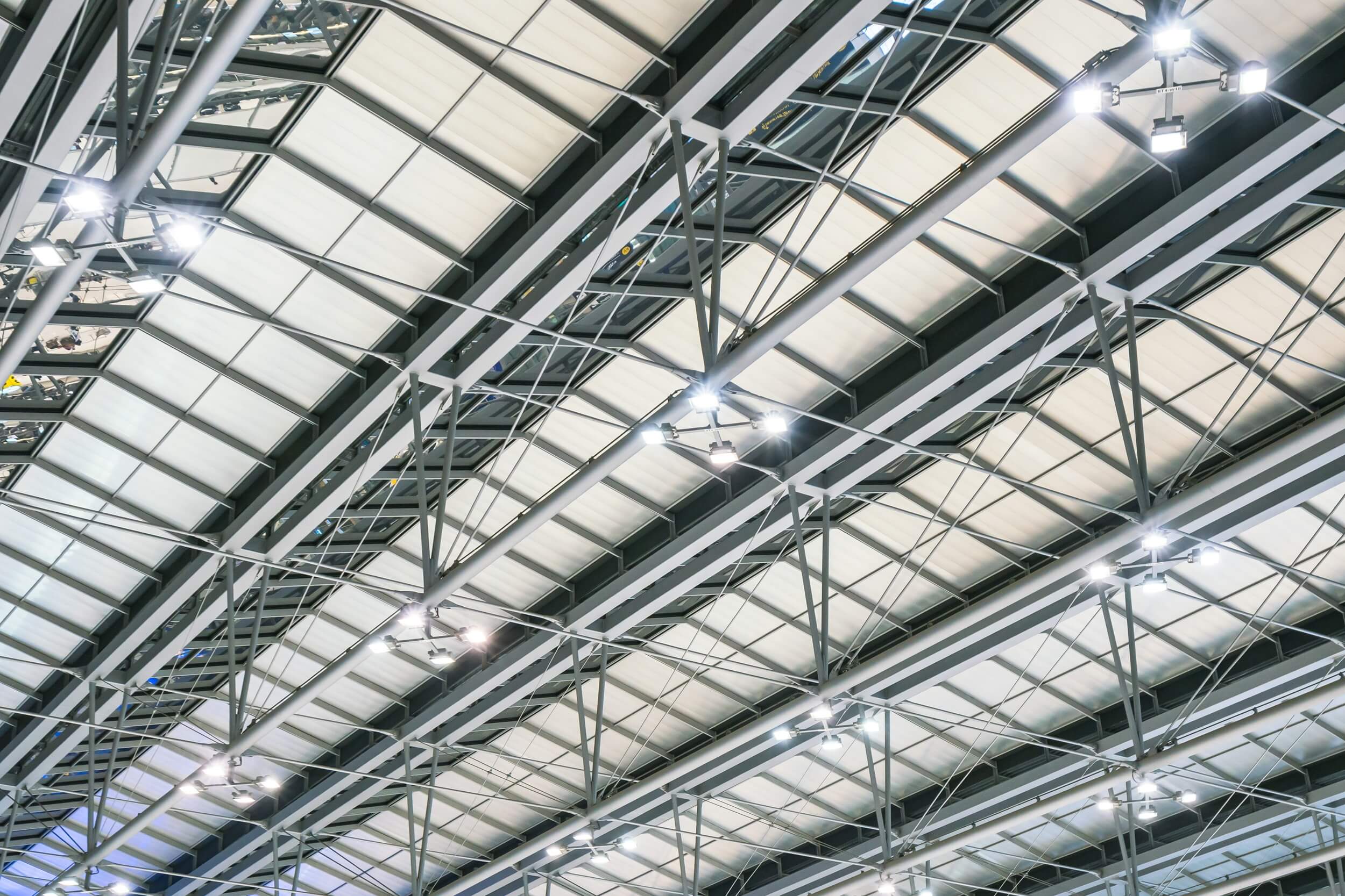 Interior view of a large commercial building roof with steel beams, skylights, and overhead lighting.