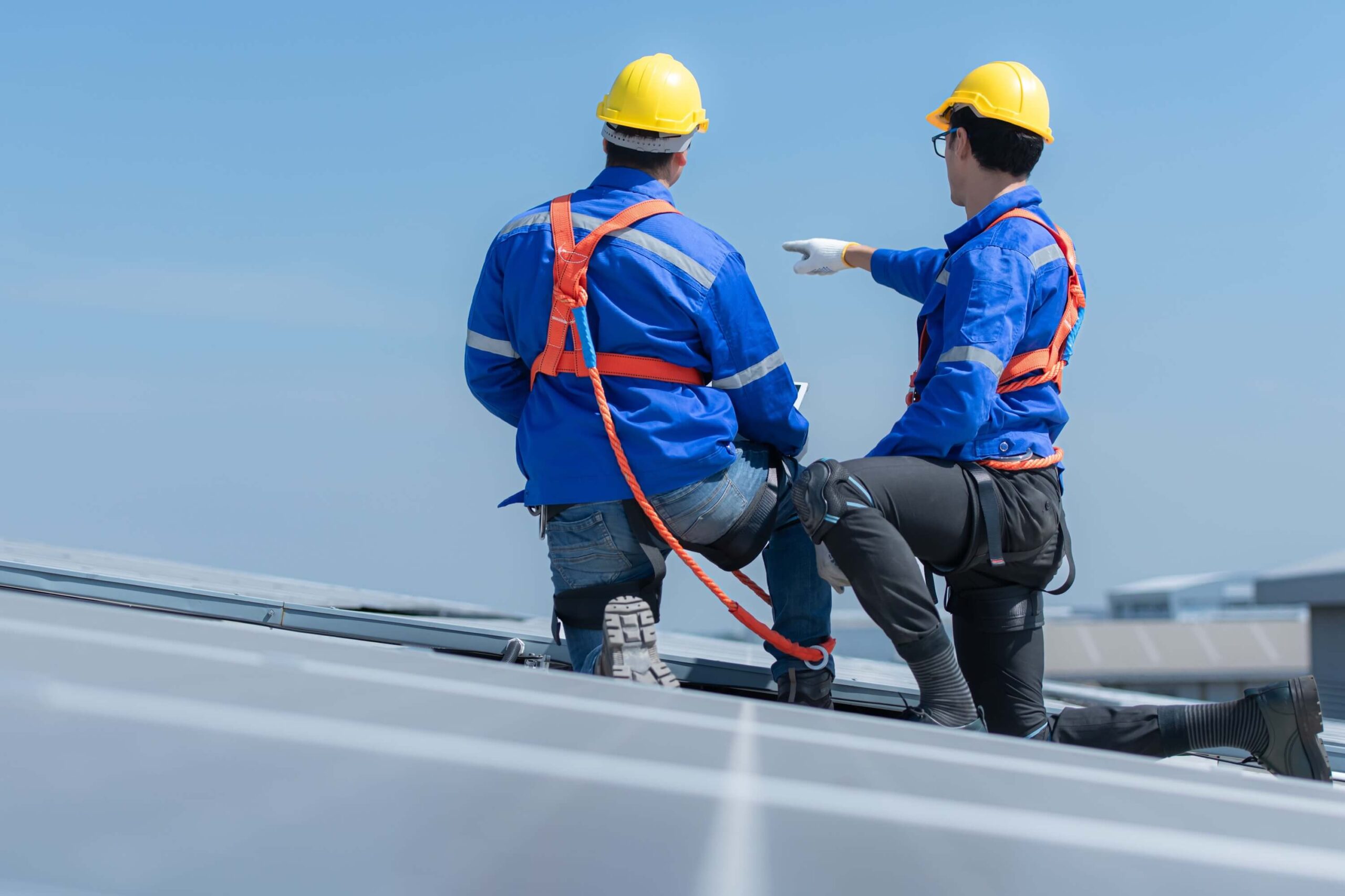 Two technicians wearing safety gear inspecting a commercial rooftop under clear skies. 