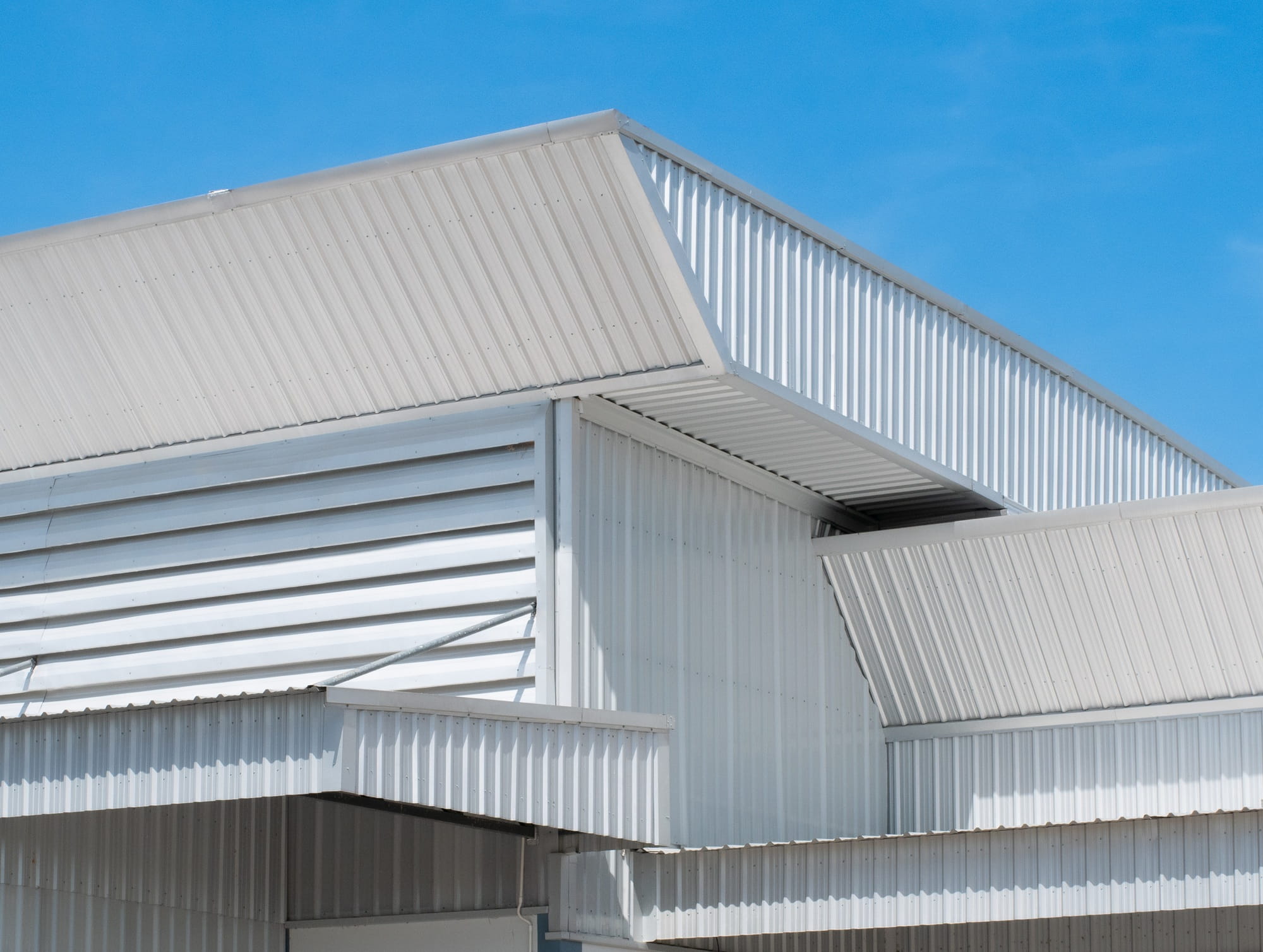 Commercial warehouse building with white metal cladding and corrugated steel roofing under a clear blue sky.
