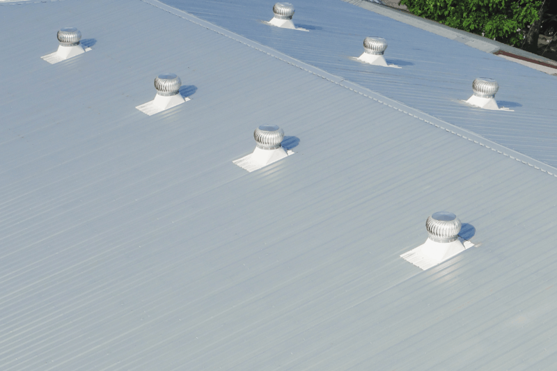 Large metal commercial roof with multiple ventilation turbines installed.