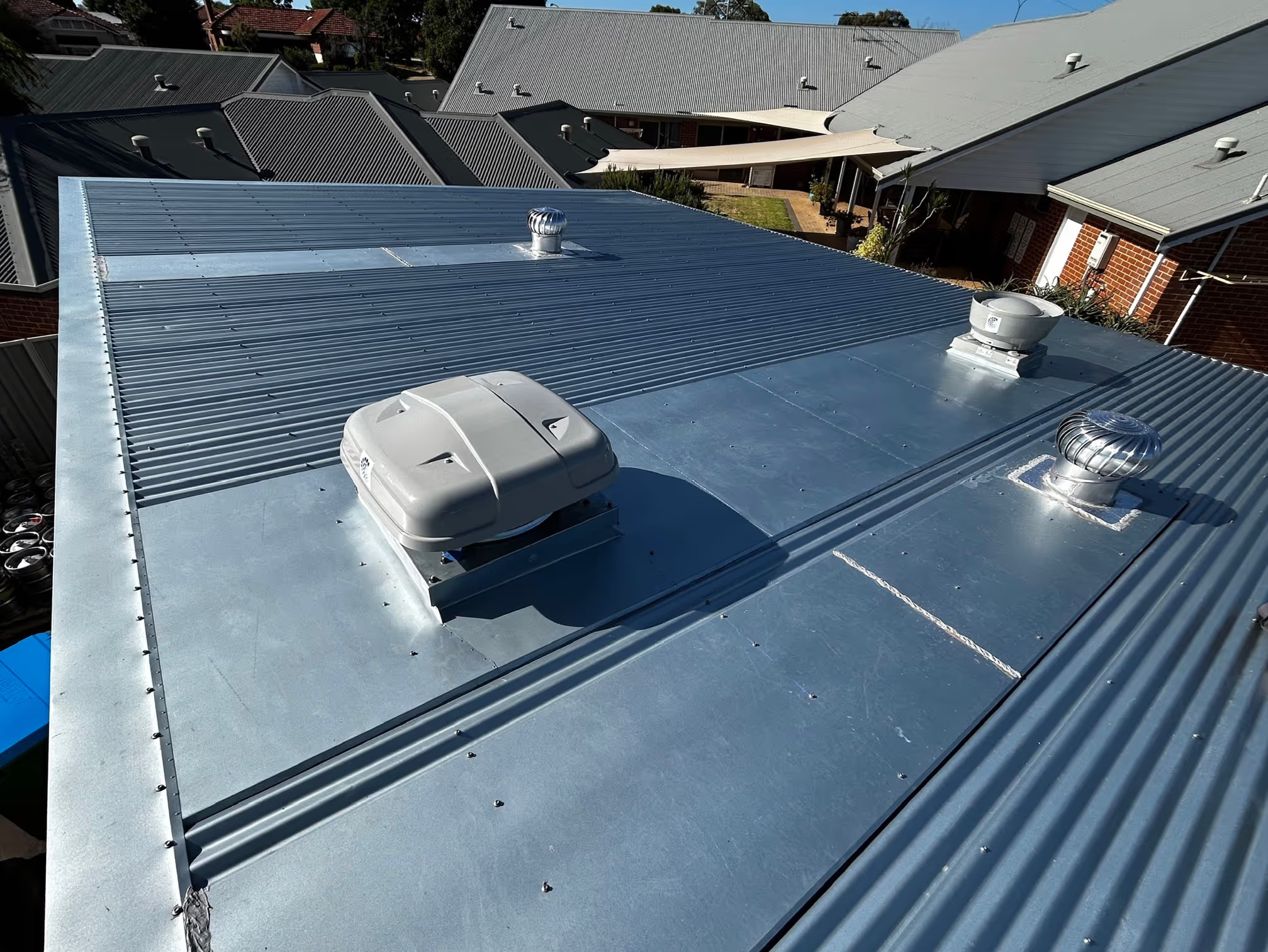 Wide view of commercial roof penetrations with exhaust ventilation units and waterproof flashing on metal roof at Baille Hill East Victoria Park.