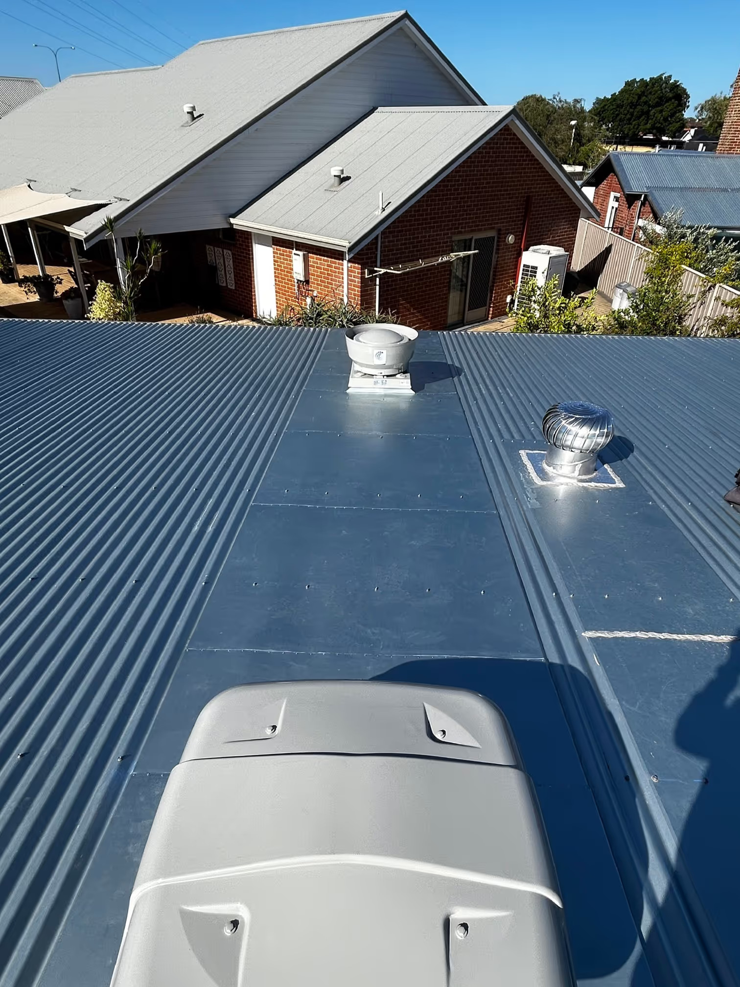 Commercial metal roof with installed exhaust fan and roof cowl penetrations, showing sealed flashing and Colorbond upstands at Baillie Hill.