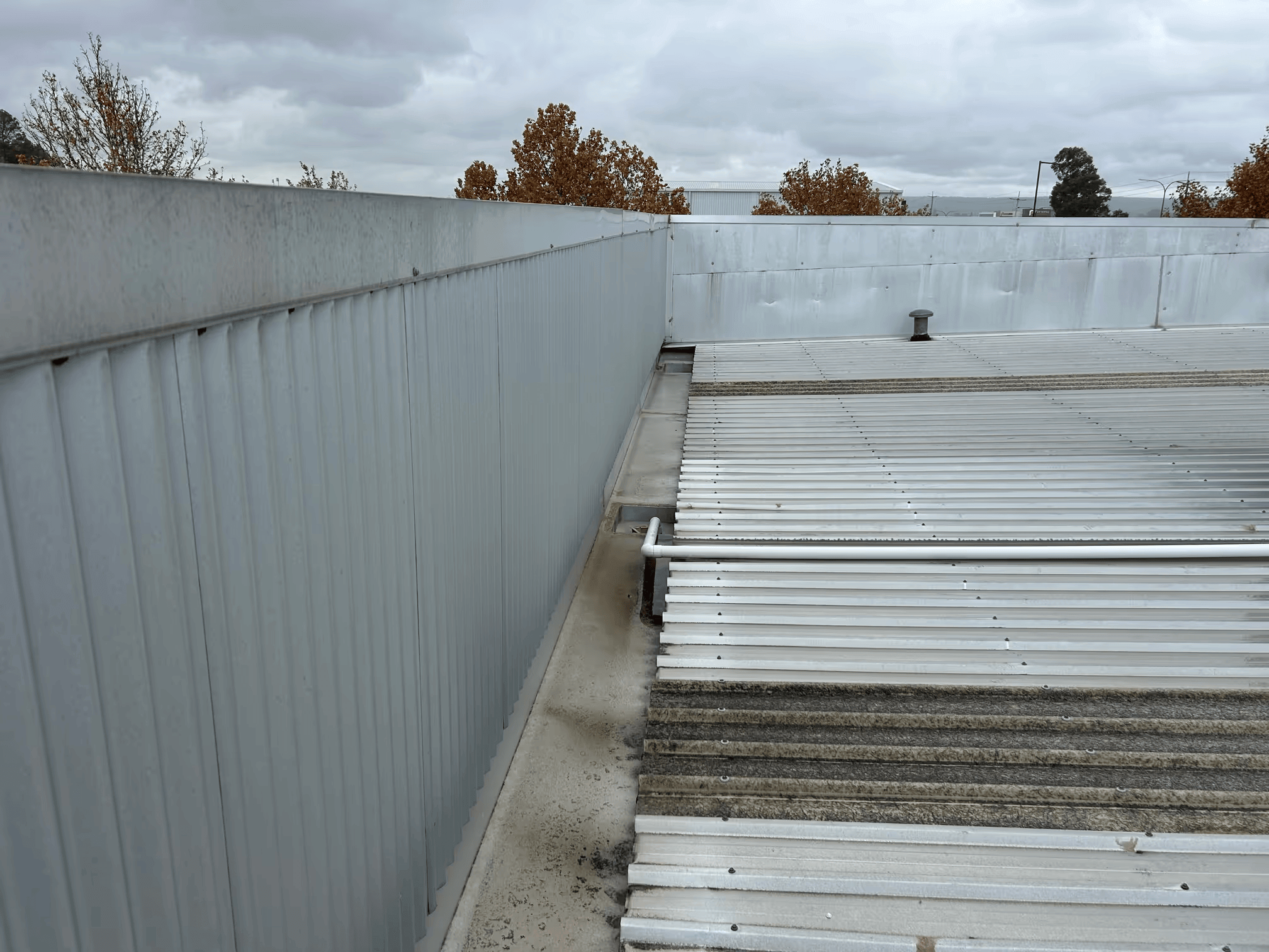 Commercial metal roof and box gutter area showing poor drainage and potential roof leak points during wet weather.
