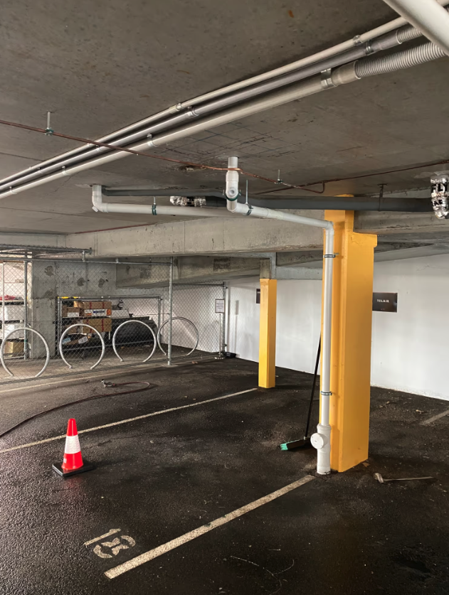 New drainage pipework installed along the ceiling and column of a commercial car park.