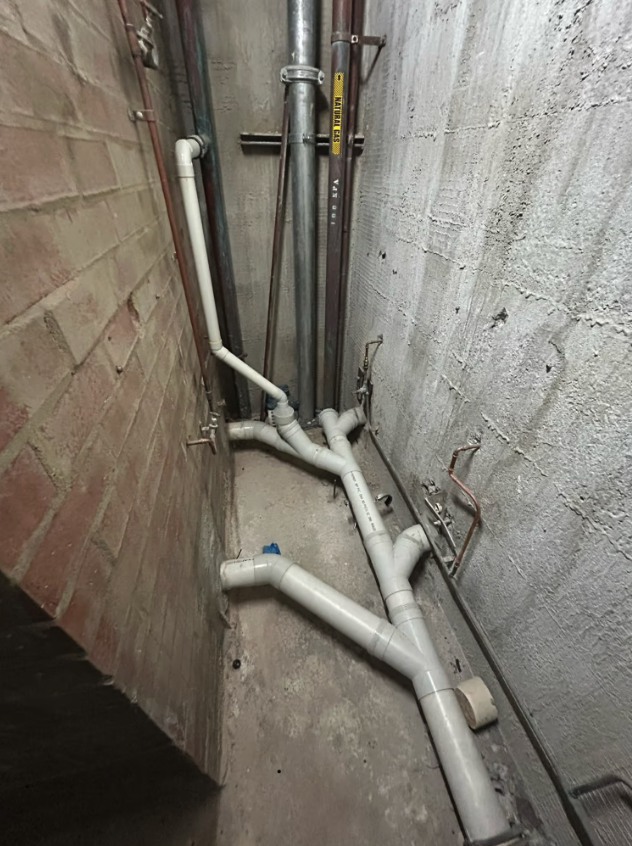 Commercial drainage pipework installed in a narrow service area between brick and concrete walls.
