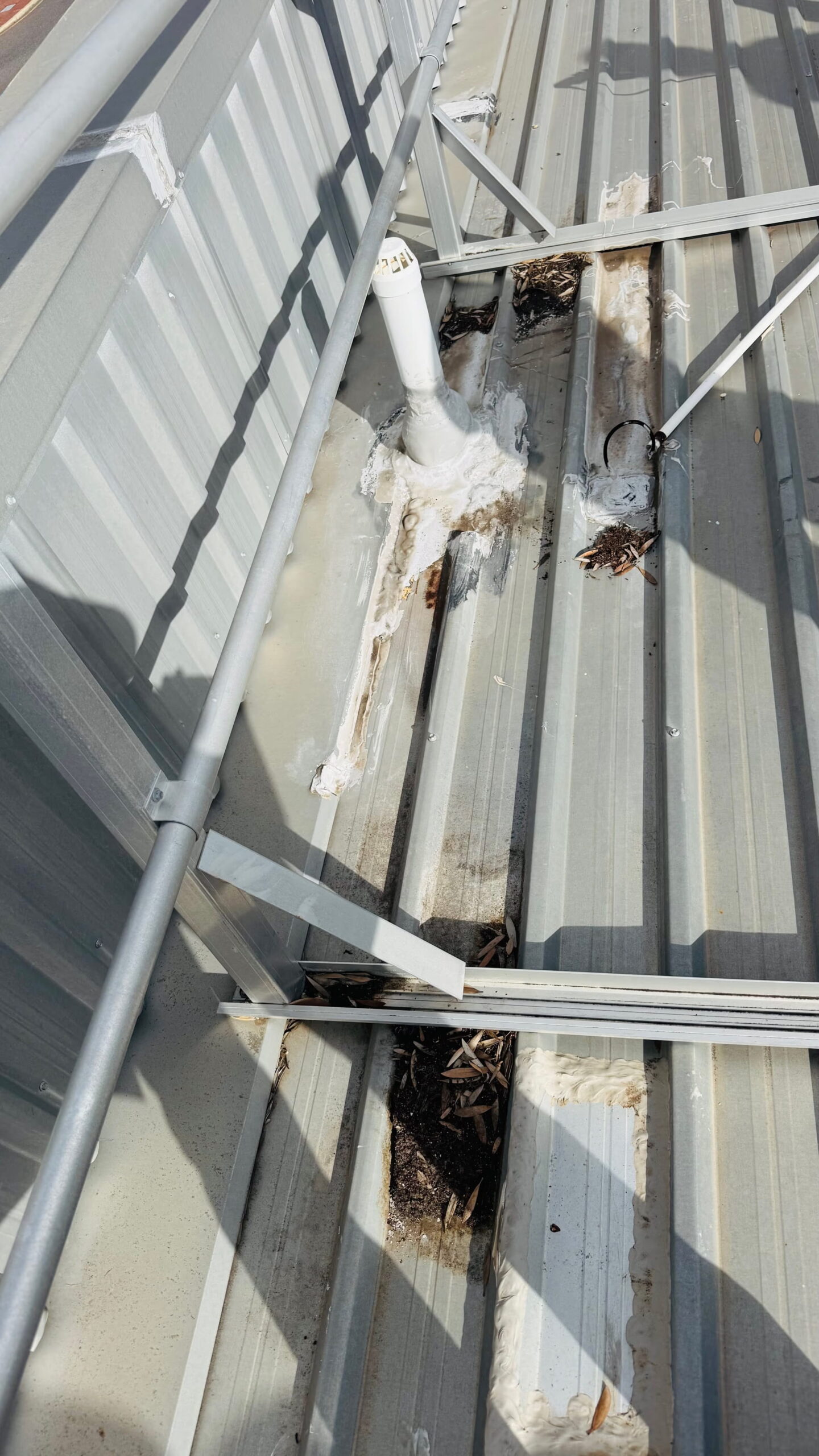 Commercial metal roof showing previous sealing around roof penetrations and accumulated debris