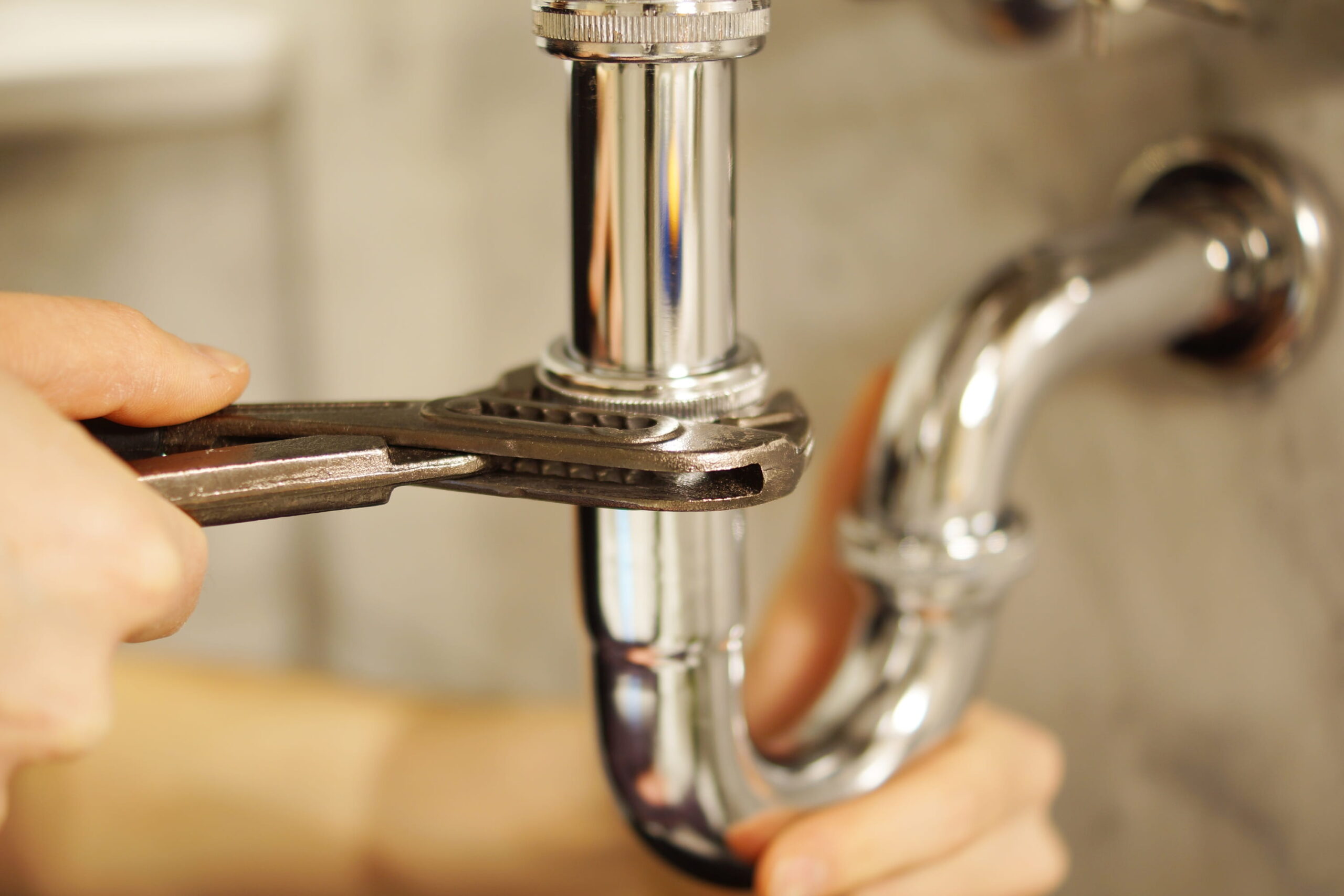 Plumber using a wrench to repair pipework beneath a sink
